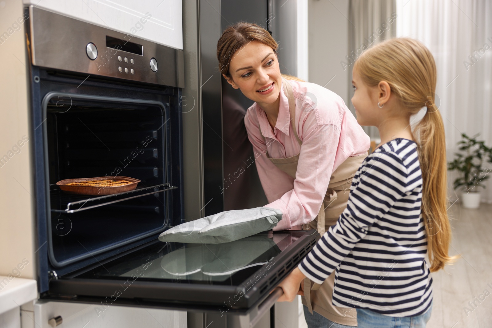 Photo of Mother and her daughter taking out pie from oven in kitchen