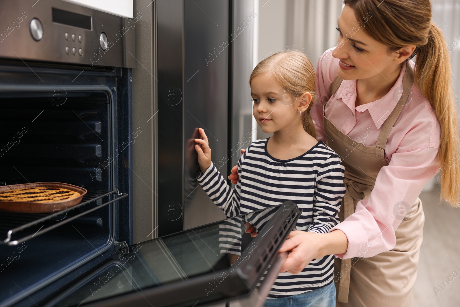 Photo of Mother and her daughter baking pie in oven indoors