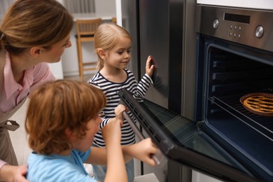 Photo of Mother and her kids baking pie in oven indoors