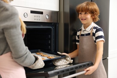 Photo of Mother and her son taking out cookies from oven in kitchen, closeup