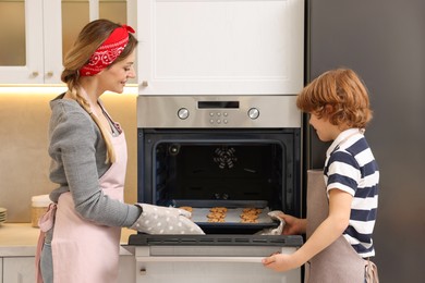 Photo of Mother and her son taking out cookies from oven in kitchen