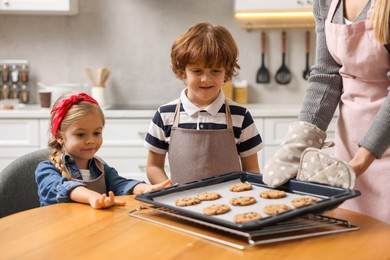 Photo of Mother and her kids with homemade cookies at wooden table in kitchen, closeup