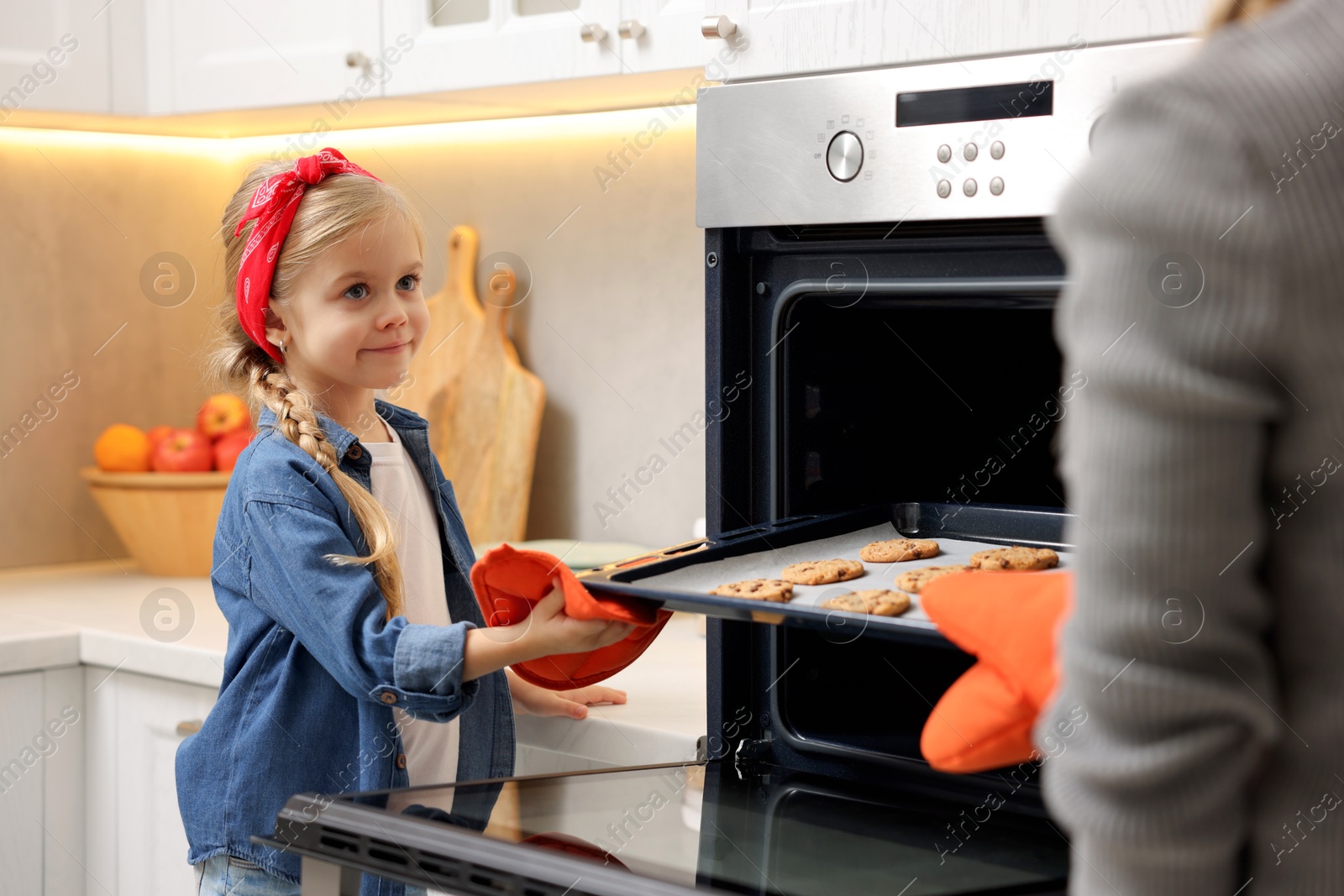 Photo of Mother and her daughter taking out buns from oven in kitchen, closeup