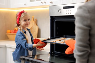 Photo of Mother and her daughter taking out buns from oven in kitchen, closeup