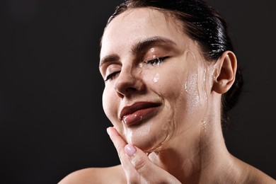 Photo of Attractive woman washing her face on black background, closeup. Space for text