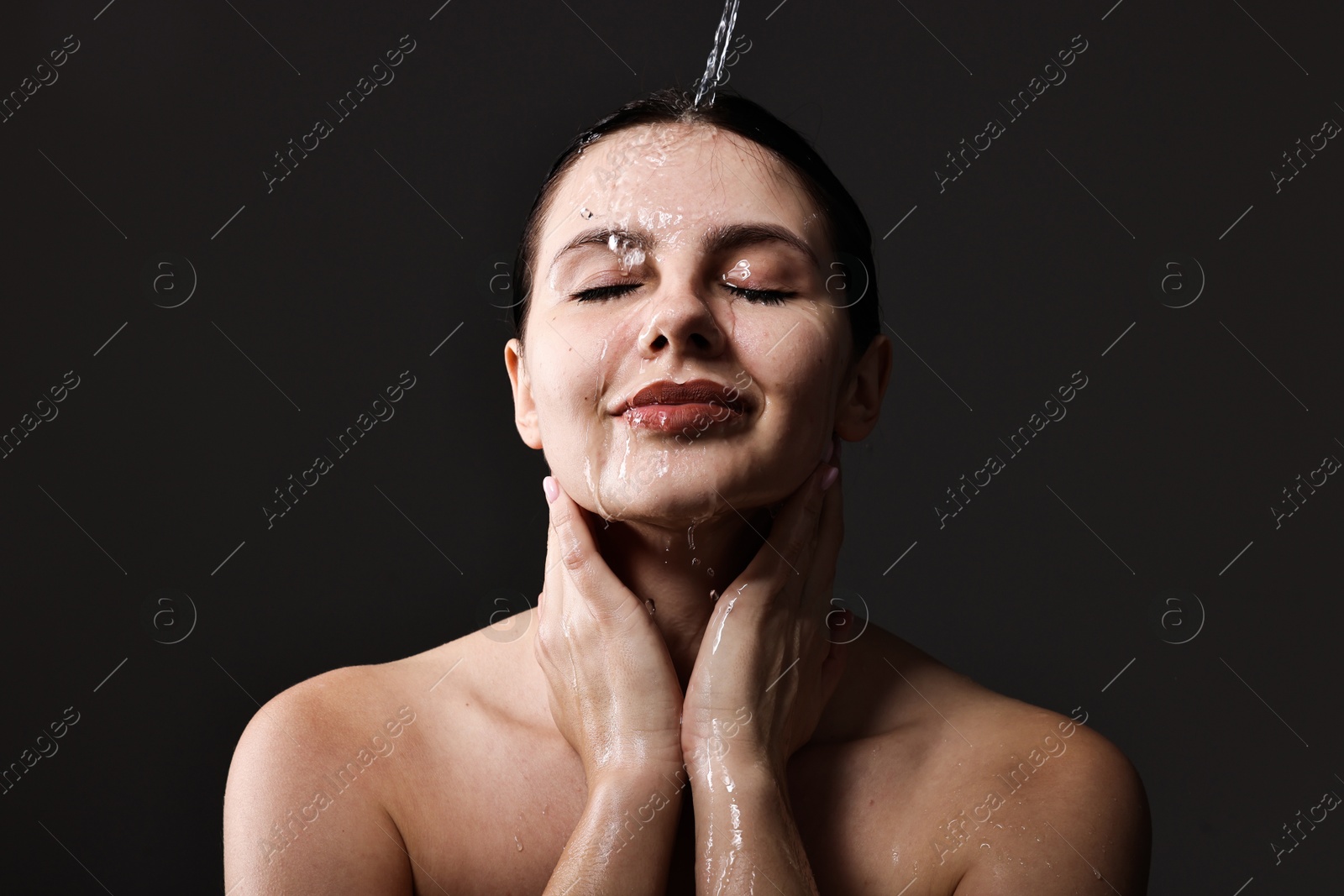 Photo of Attractive woman washing her face on black background