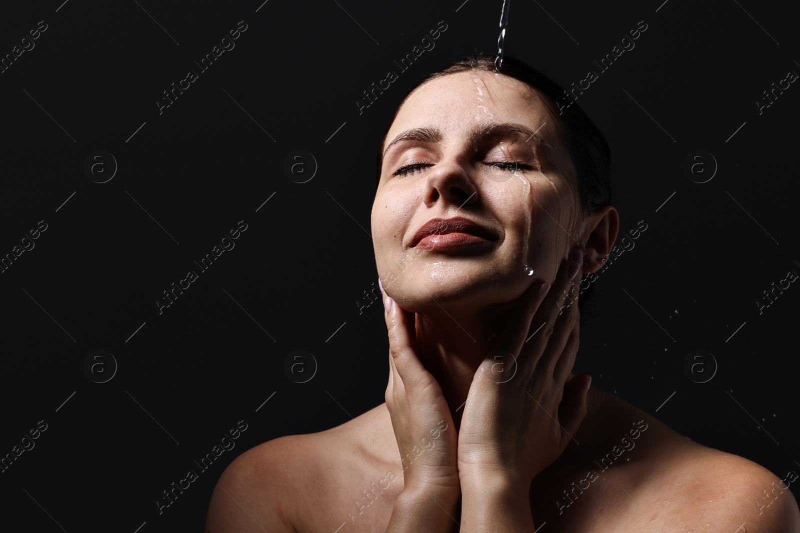 Photo of Attractive woman washing her face on black background