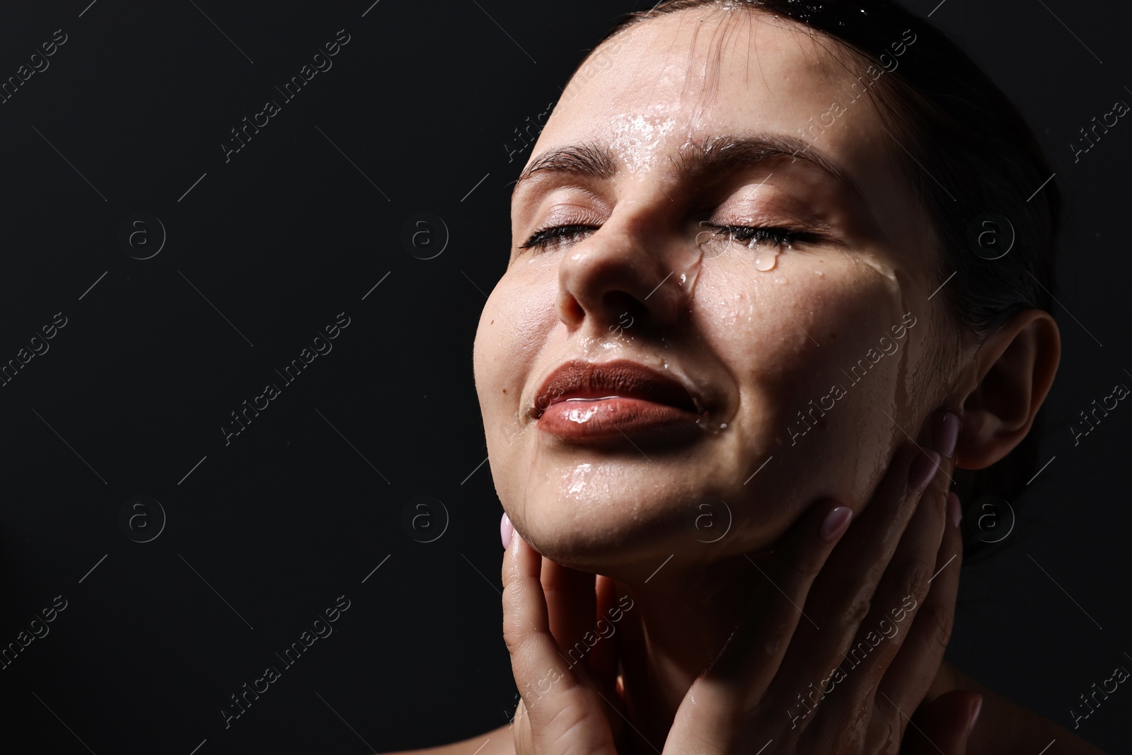 Photo of Attractive woman washing her face on black background, closeup. Space for text