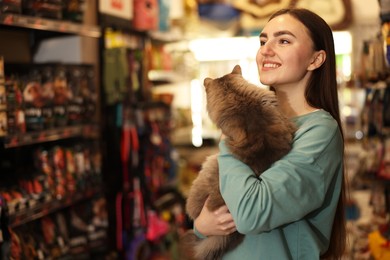 Photo of Happy woman with her cute cat in pet shop. Space for text