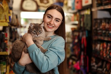 Photo of Happy woman with her cute cat in pet shop. Space for text