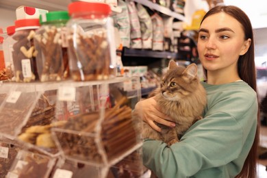 Photo of Woman choosing treats for her cute cat in pet shop