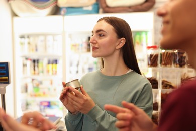 Photo of Pet shop worker helping woman choosing food indoors, selective focus