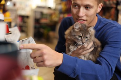 Photo of Man with his cute cat in pet shop, closeup