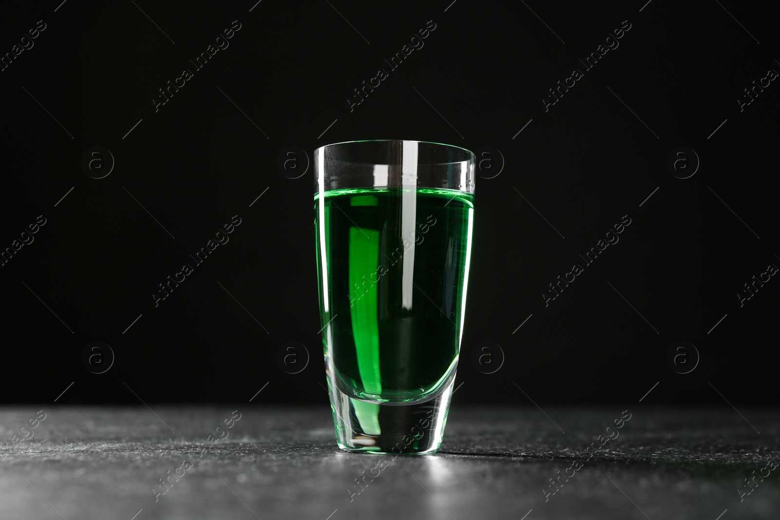 Photo of Absinthe in shot glass on table against black background, low angle view