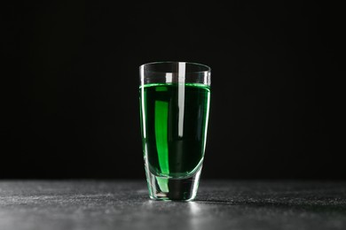 Photo of Absinthe in shot glass on table against black background, low angle view