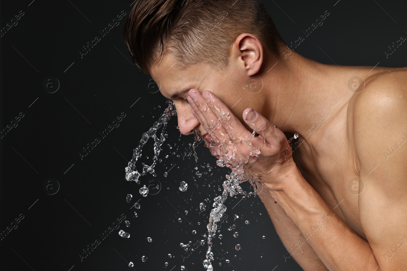 Photo of Man washing his face on black background. Space for text