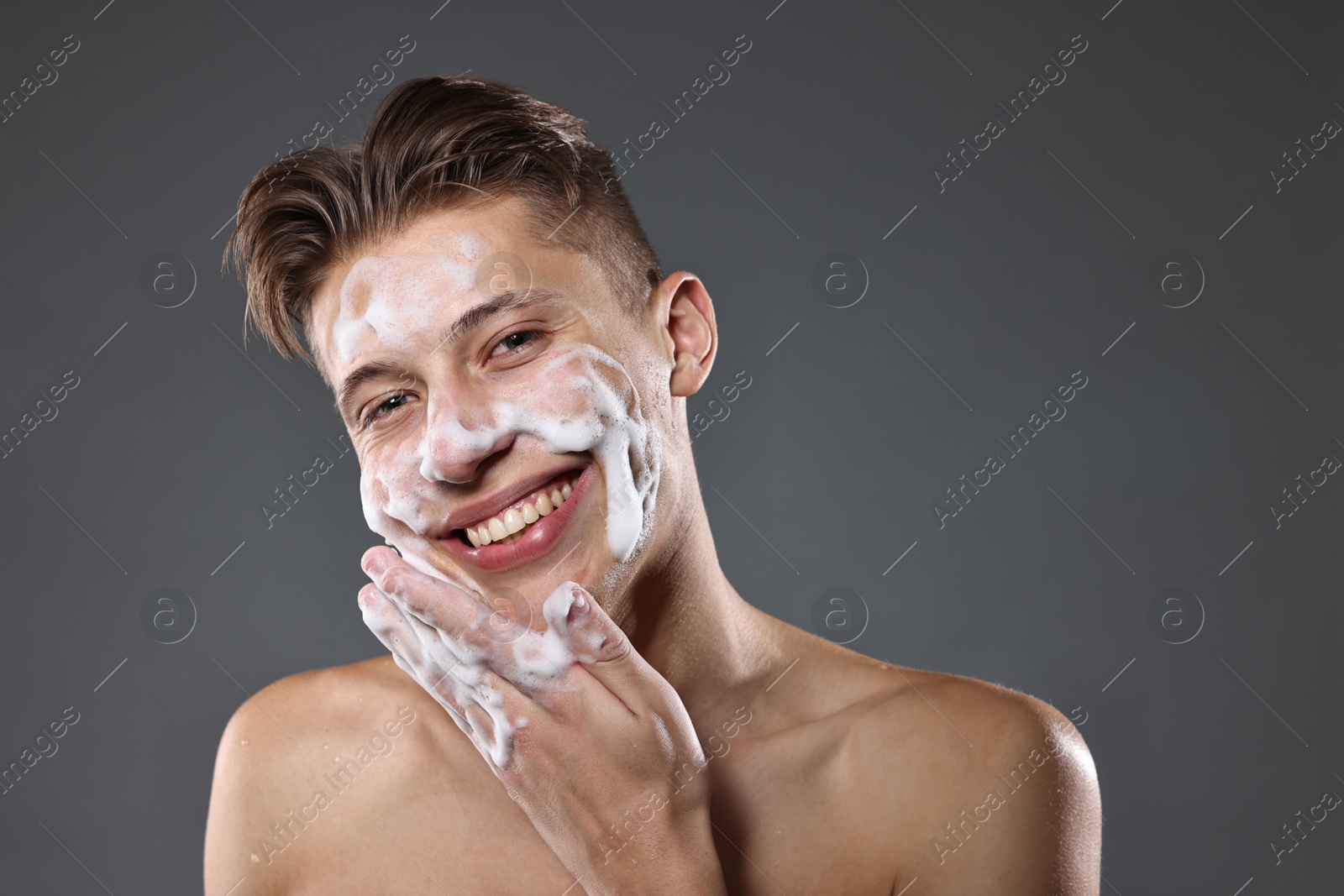 Photo of Smiling man washing his face with cleansing foam on grey background