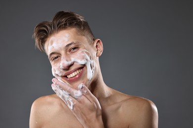 Photo of Smiling man washing his face with cleansing foam on grey background