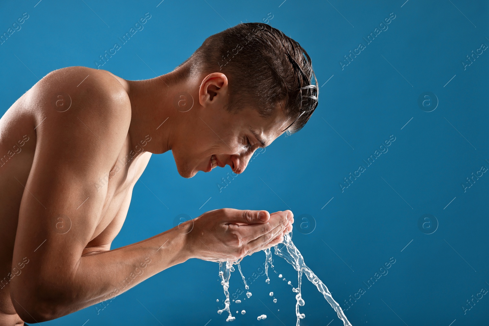 Photo of Smiling man washing his face on blue background. Space for text