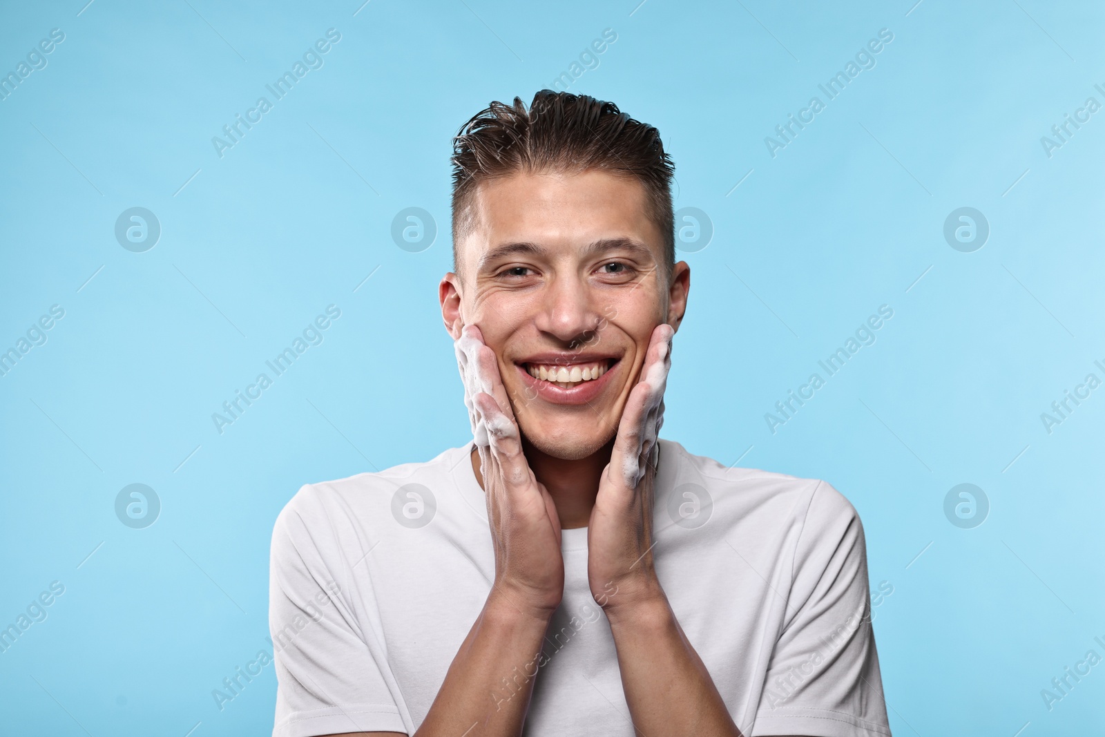 Photo of Smiling man washing his face with cleansing foam on light blue background