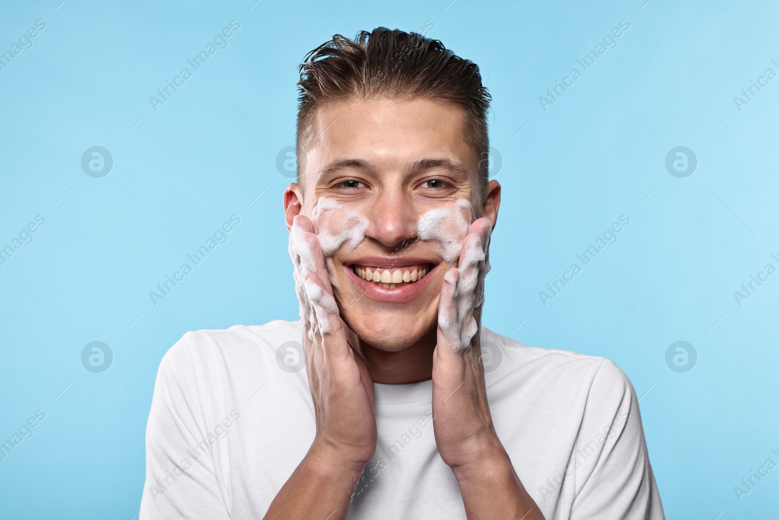 Photo of Smiling man washing his face with cleansing foam on light blue background