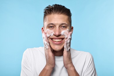 Photo of Smiling man washing his face with cleansing foam on light blue background