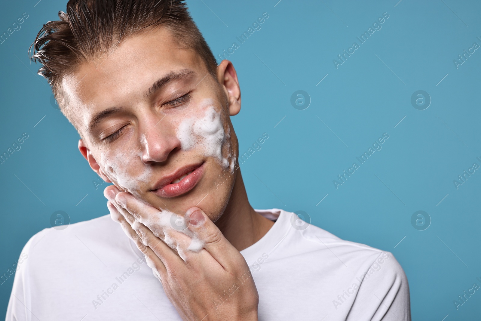 Photo of Handsome man washing his face with cleansing foam on blue background