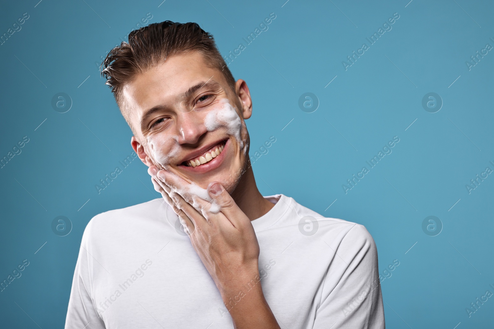 Photo of Smiling man washing his face with cleansing foam on blue background