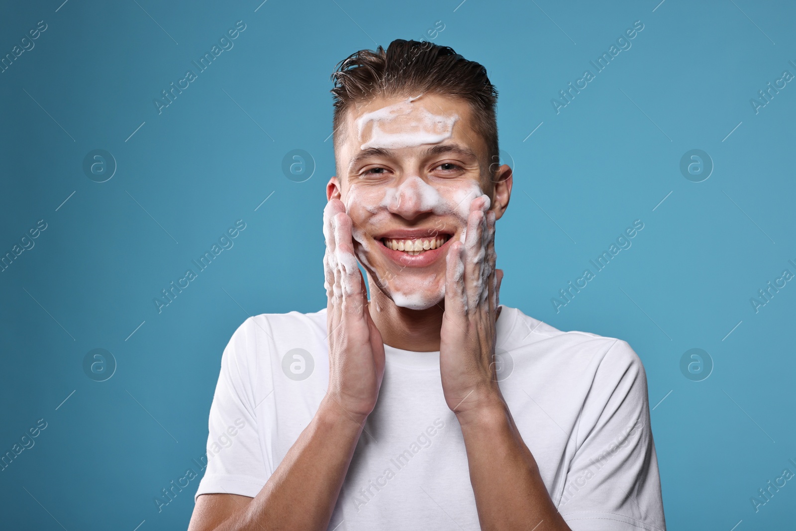 Photo of Smiling man washing his face with cleansing foam on blue background