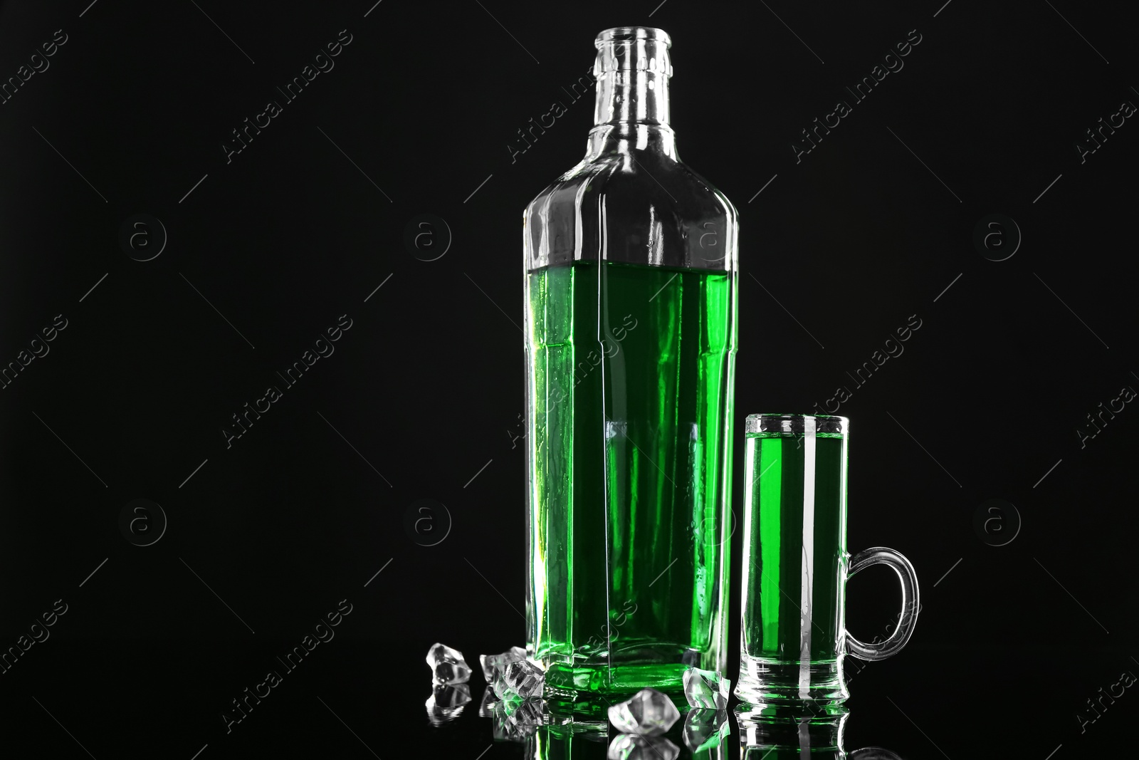 Photo of Absinthe in shot glass, bottle and ice cubes on black mirror surface, space for text