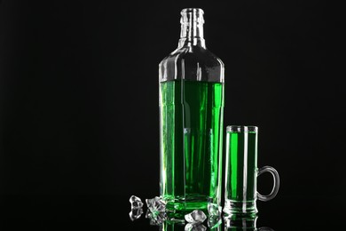 Photo of Absinthe in shot glass, bottle and ice cubes on black mirror surface, space for text