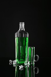 Photo of Absinthe in shot glass, bottle and ice cubes on black mirror surface