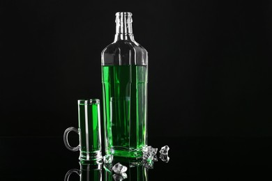 Photo of Absinthe in shot glass, bottle and ice cubes on black mirror surface, space for text