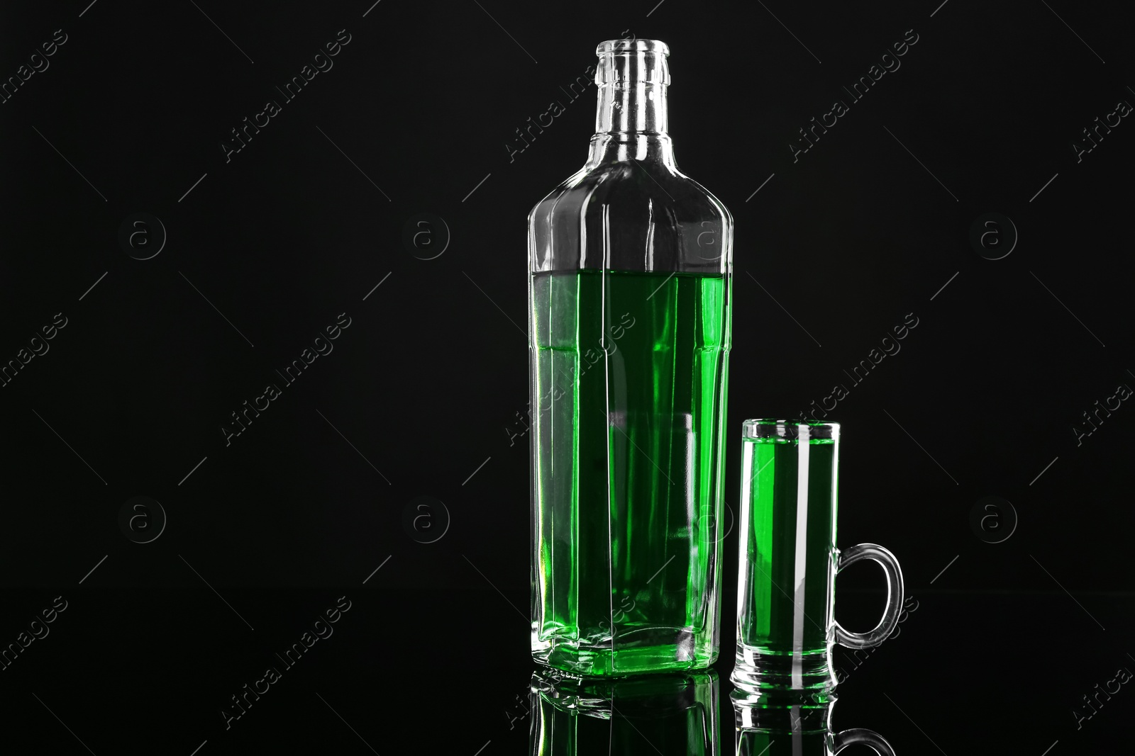 Photo of Absinthe in shot glass and bottle on black mirror surface, space for text