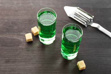 Photo of Absinthe in shot glasses, brown sugar and slotted spoon on wooden table, closeup