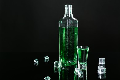 Photo of Absinthe in shot glass, bottle and ice cubes on black mirror surface, space for text