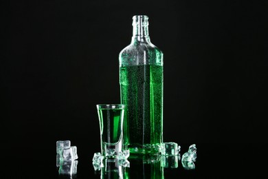 Photo of Absinthe in shot glass, bottle and ice cubes on black mirror surface