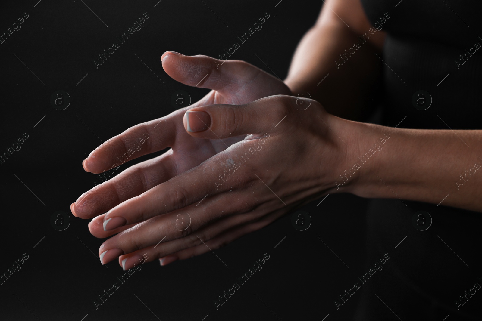 Photo of Woman with talcum powder on her hands before training against black background, closeup