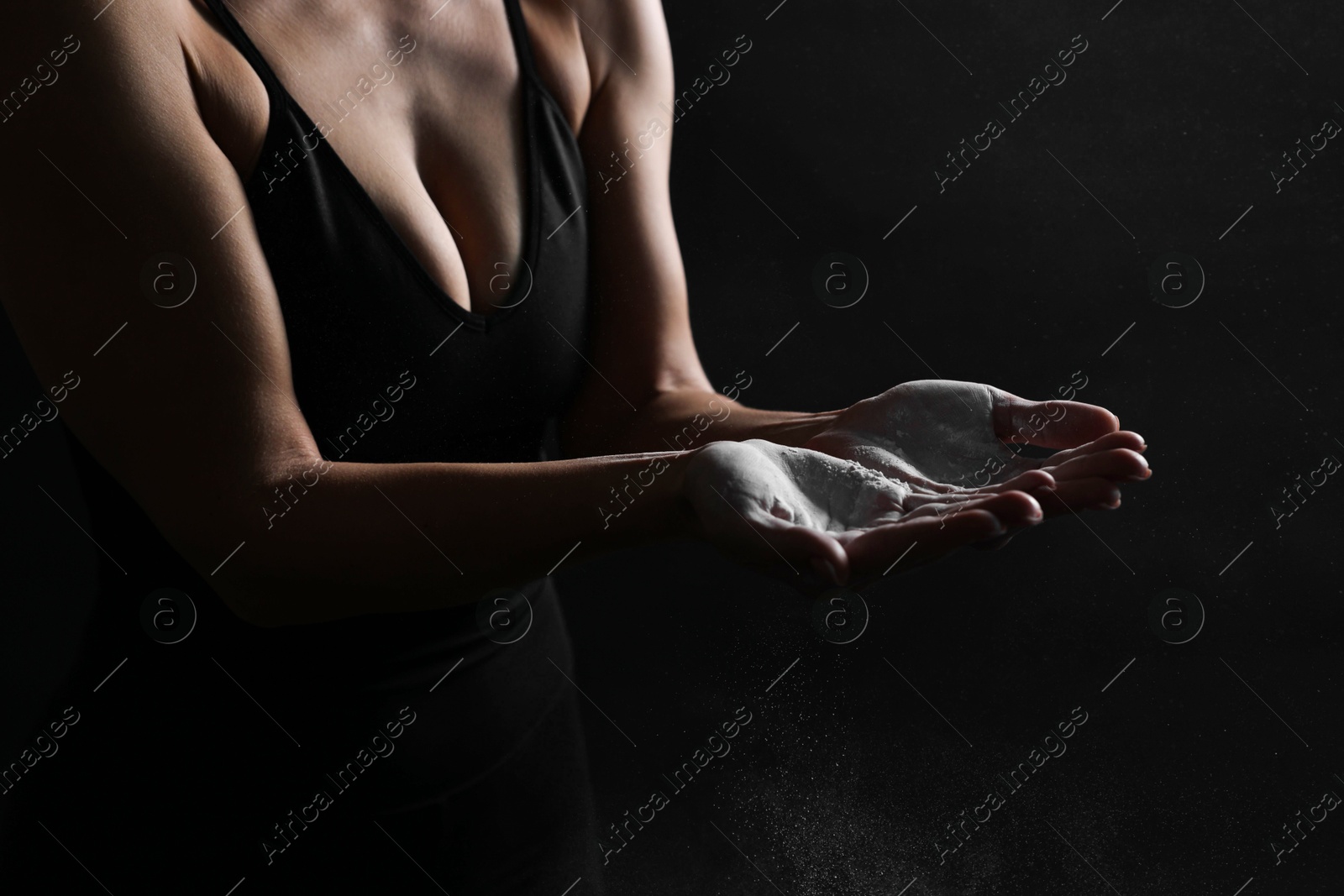 Photo of Woman with talcum powder on her hands before training against black background, closeup