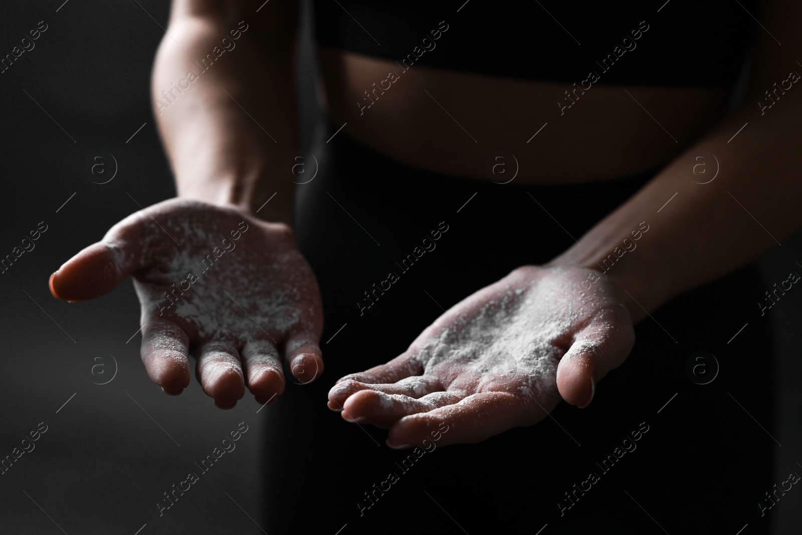 Photo of Woman with talcum powder on her hands before training against black background, closeup