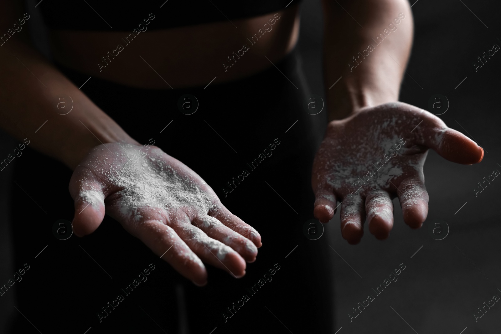 Photo of Woman with talcum powder on her hands before training against black background, closeup