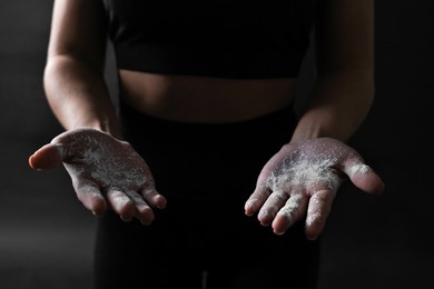 Photo of Woman with talcum powder on her hands before training against black background, closeup