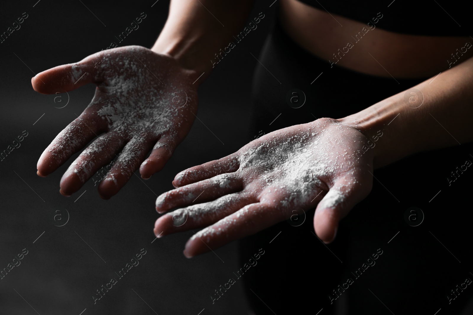 Photo of Woman with talcum powder on her hands before training against black background, closeup