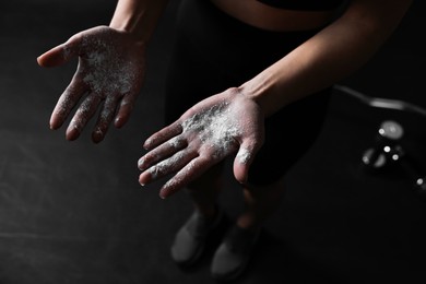 Photo of Woman with talcum powder on her hands before training against black background, closeup