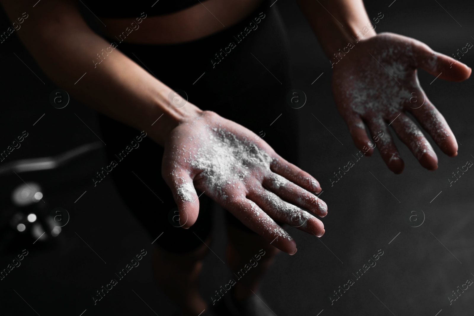 Photo of Woman with talcum powder on her hands before training against black background, closeup