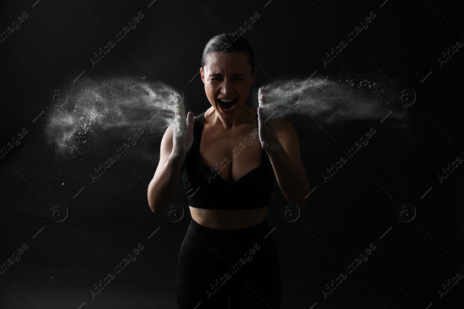 Photo of Woman clapping hands with talcum powder before training on black background