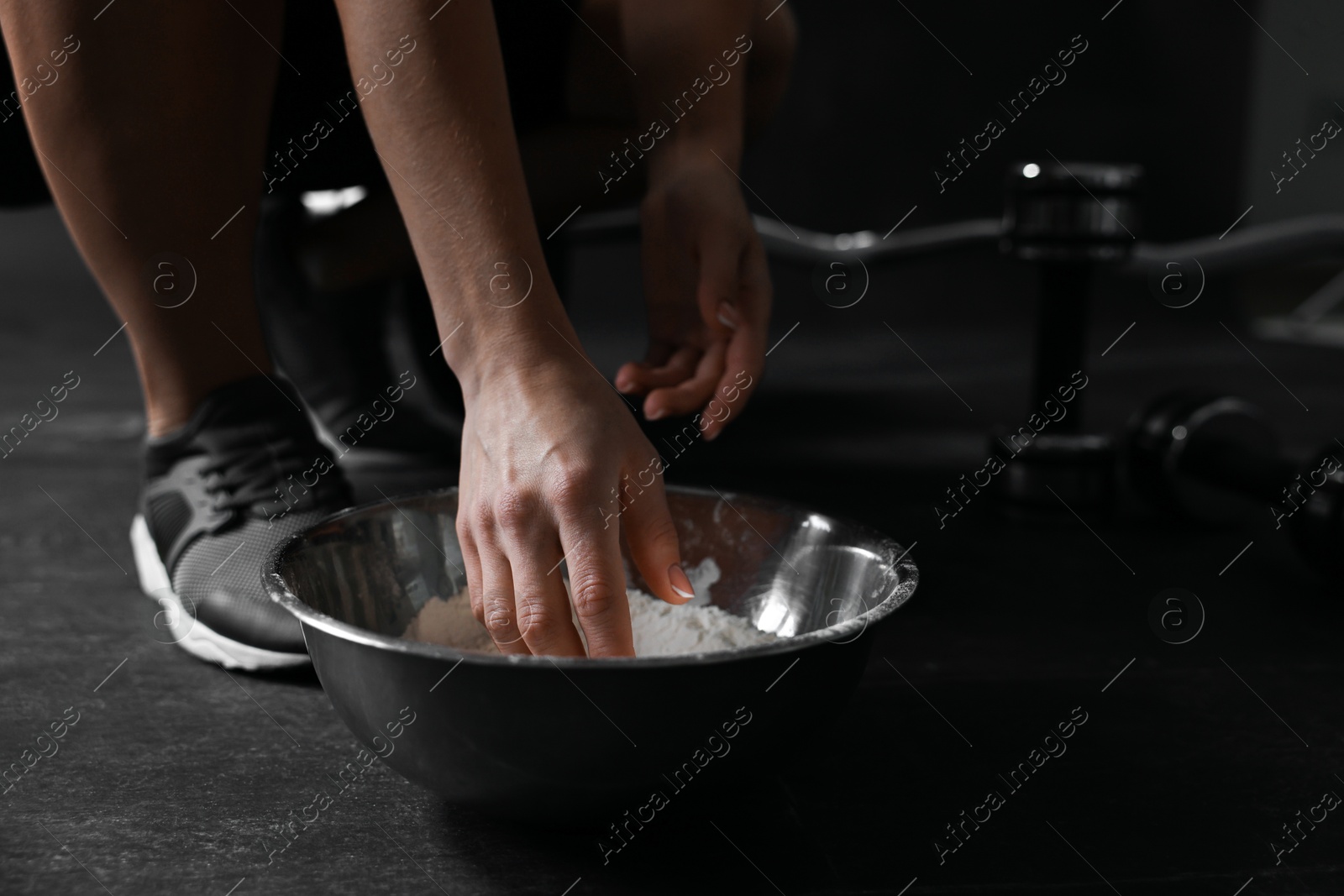 Photo of Woman applying talcum powder onto her hands above bowl before training in gym, closeup