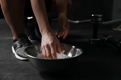 Photo of Woman applying talcum powder onto her hands above bowl before training in gym, closeup