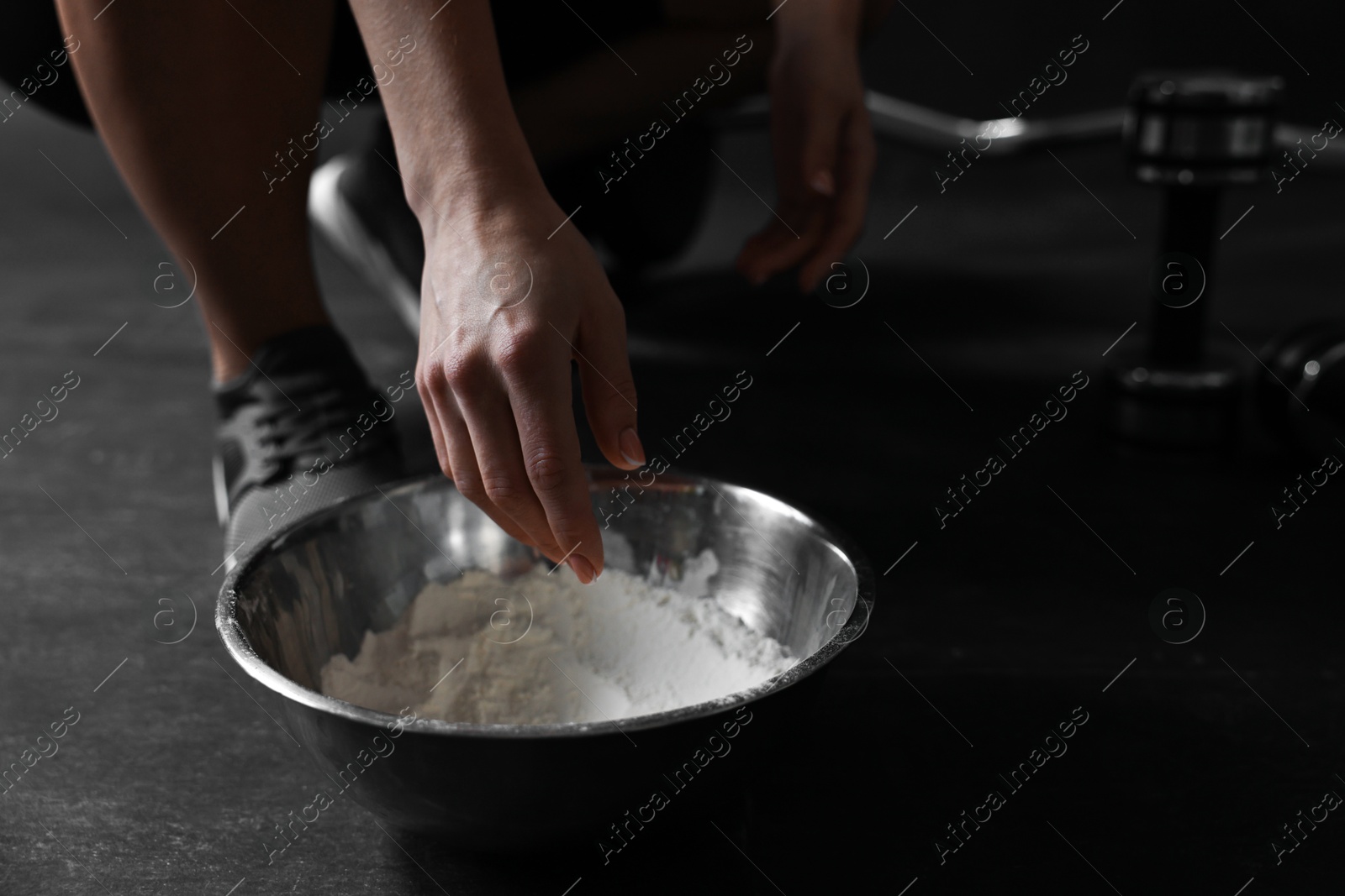 Photo of Woman applying talcum powder onto her hands above bowl before training in gym, closeup