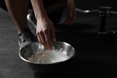 Photo of Woman applying talcum powder onto her hands above bowl before training in gym, closeup